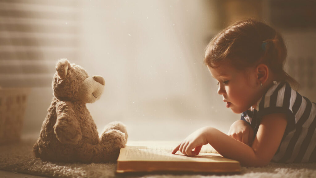 Young girl reading a book with a teddy